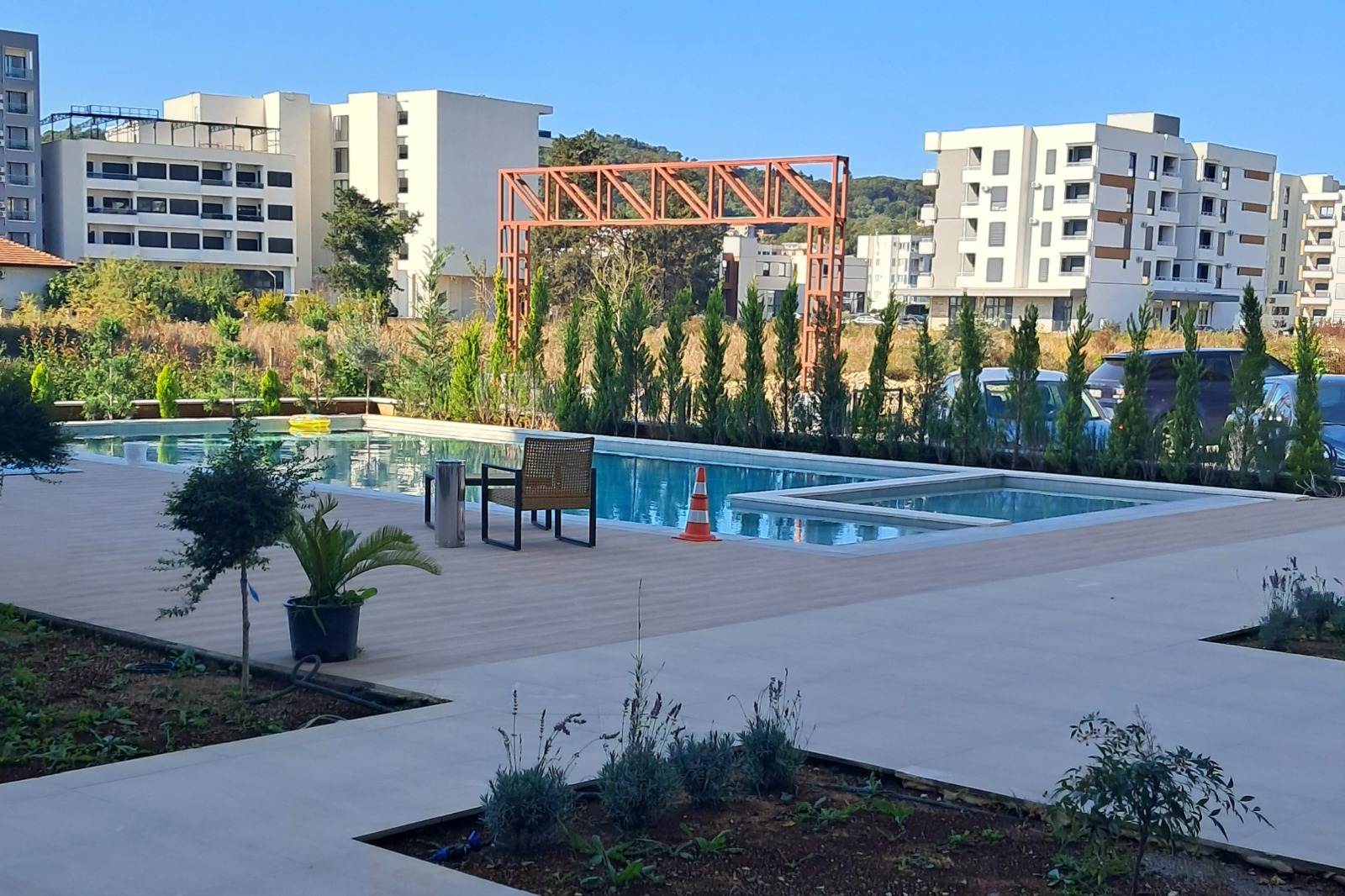 Luxurious Ulcinj pool area with lounge chairs, lush greenery, and modern apartments&mdash;exclusive listings on immobilien.ekosphere.me by Ekosphere DOO.